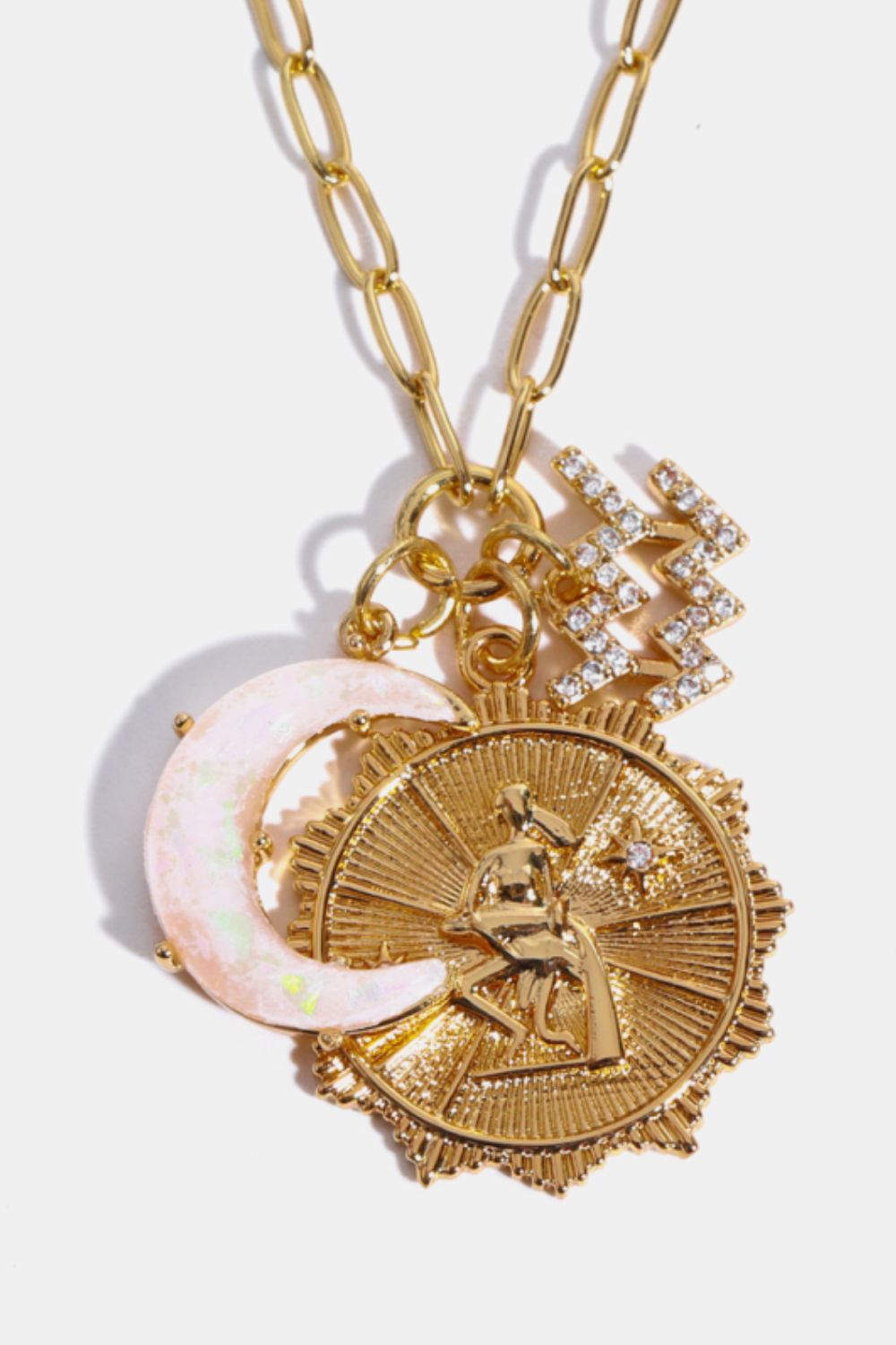 Gold pendant necklace with celestial charms: zodiac sign, moon, and starburst medallion.