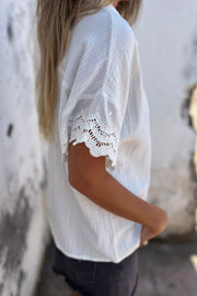 White cotton blouse with textured fabric and eyelet lace trim on the short sleeves.