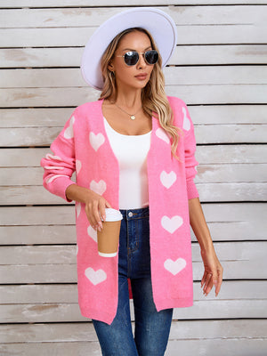 Pink acrylic cardigan with white intarsia hearts, long sleeves, open front, and relaxed fit.