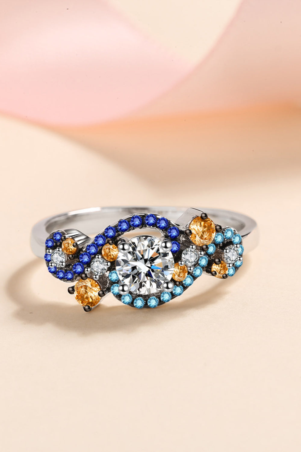 Silver ring with a central diamond and swirling blue, gold, and clear gemstones.