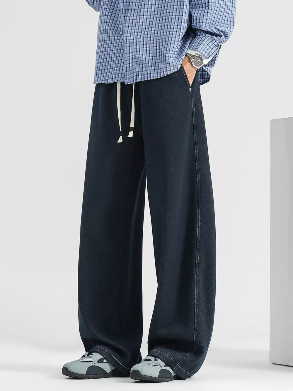 Men's dark wash loose fit drawstring jeans with white ties and side stitching.