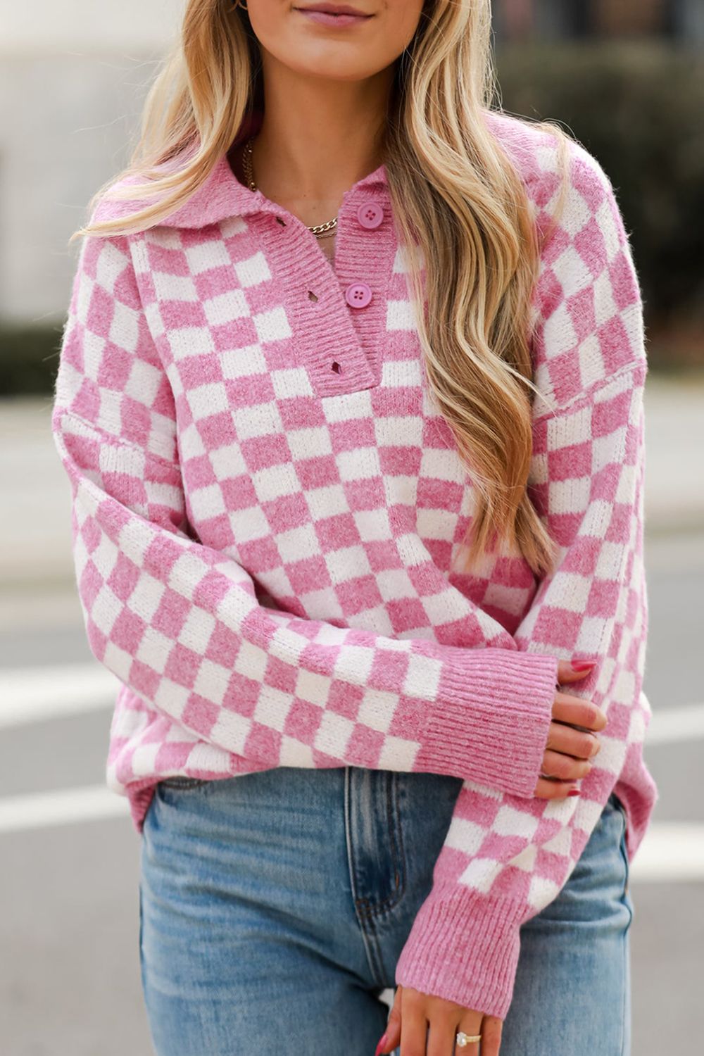 Pink checkerboard knit polo sweater with button detail and collared neckline.