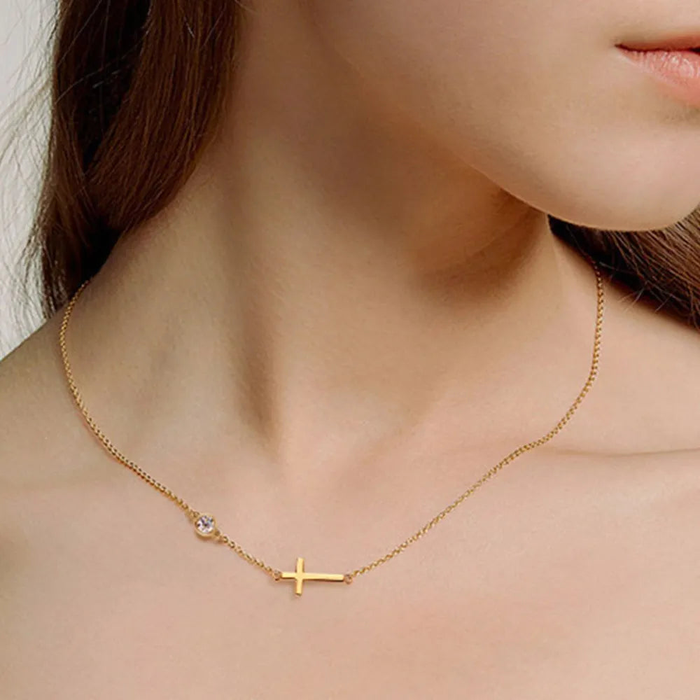 Gold asymmetrical cross pendant necklace with a single clear stone.