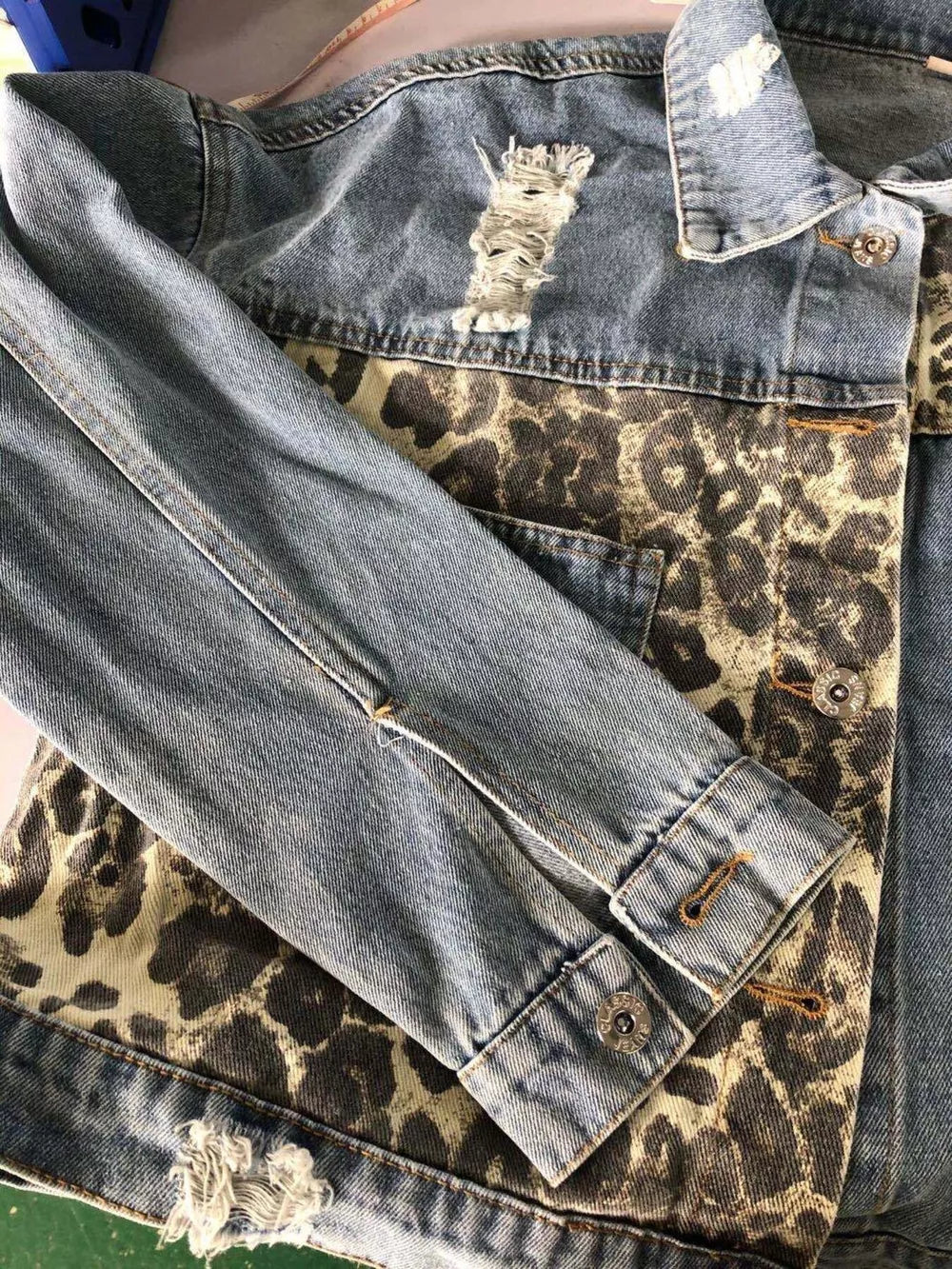 Distressed denim trucker jacket with leopard print panels and button cuffs.
