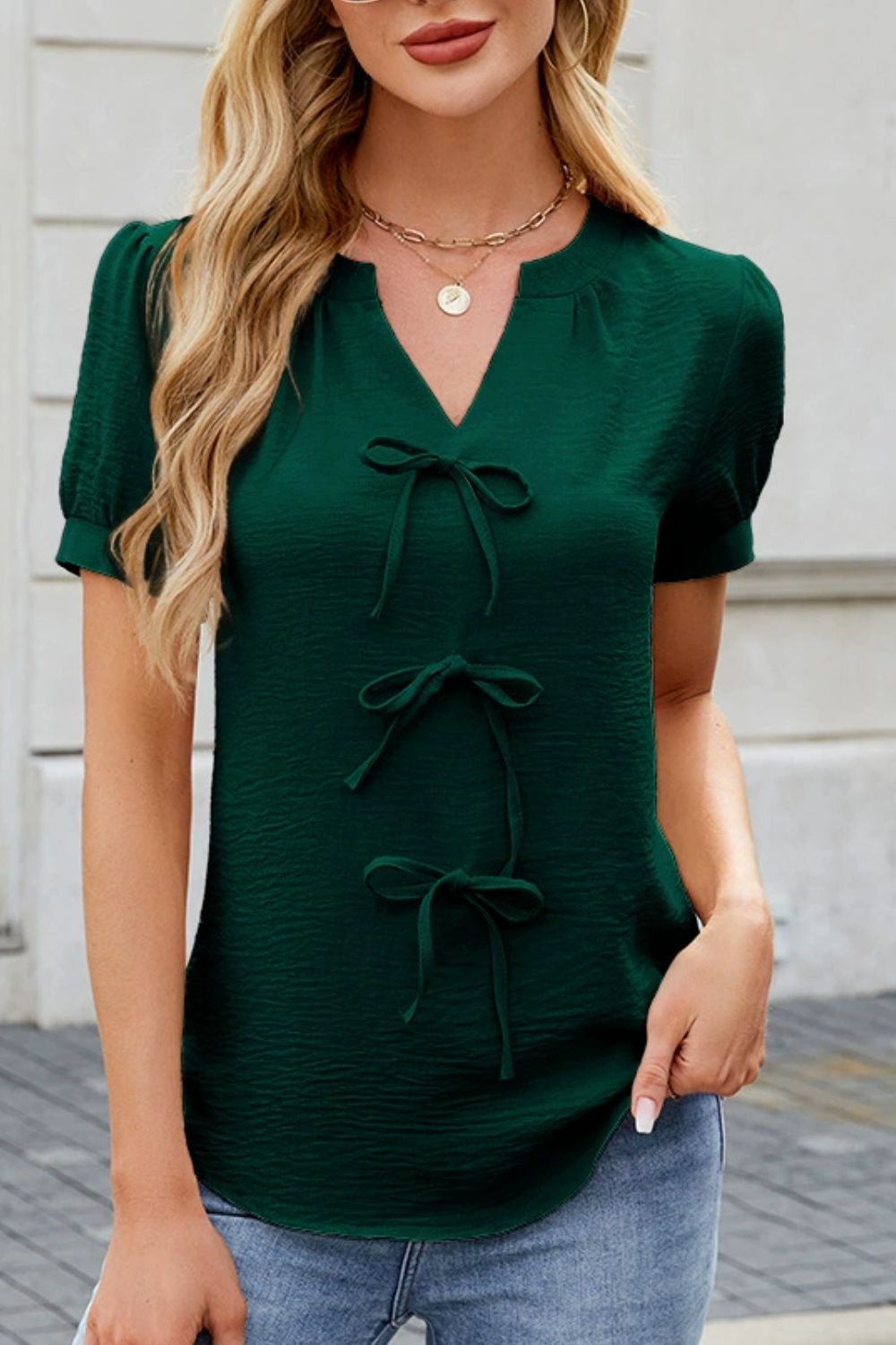 Dark green textured V-neck blouse with three bow details and short puff sleeves.