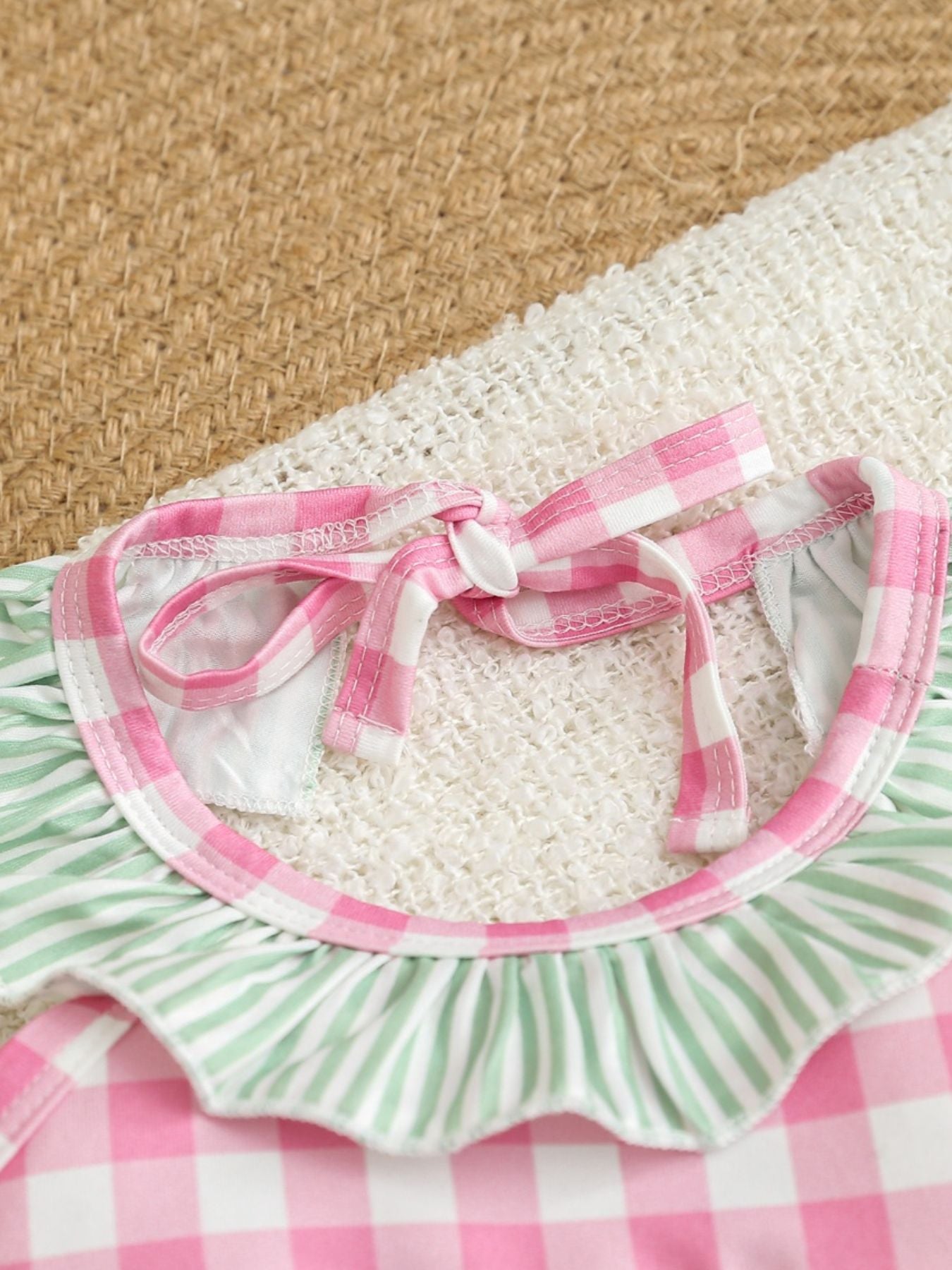Baby one-piece swimsuit with pink gingham and green stripes, featuring ruffle trim and tie straps.