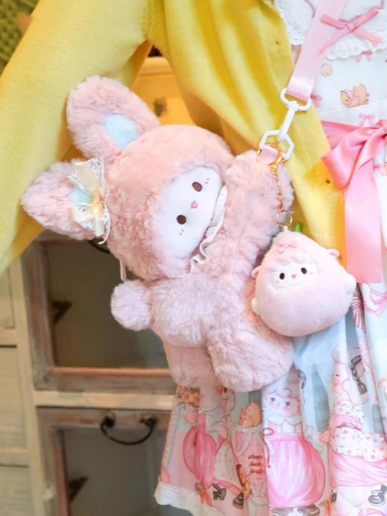Pink plush bunny backpack with lace trim and a small sheep charm, attached to a pink strap.