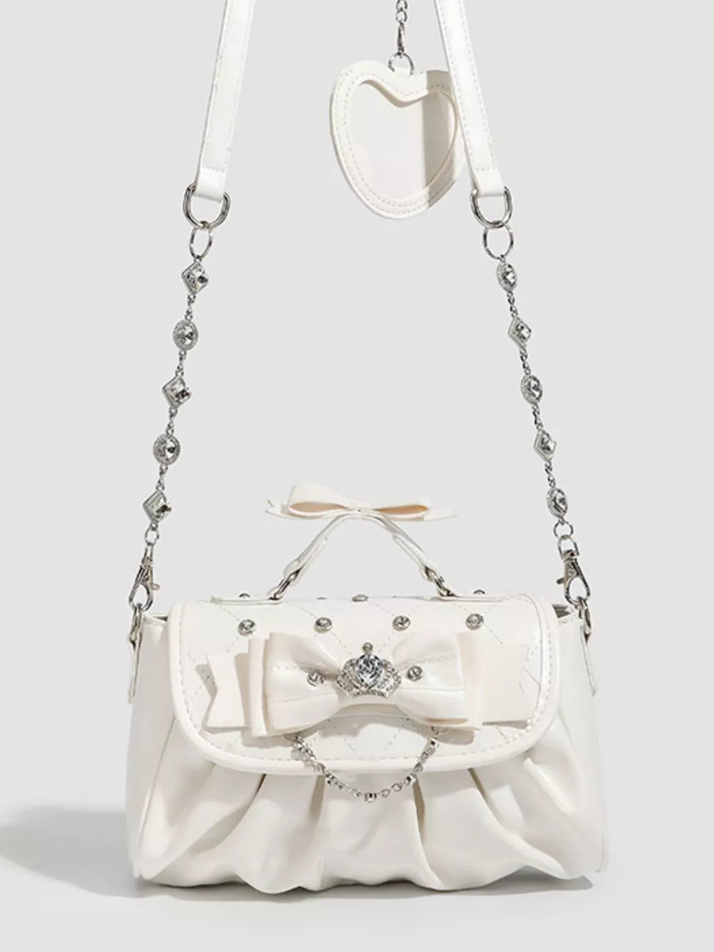 White ruched crossbody bag with bow, crown charm, and chain strap.