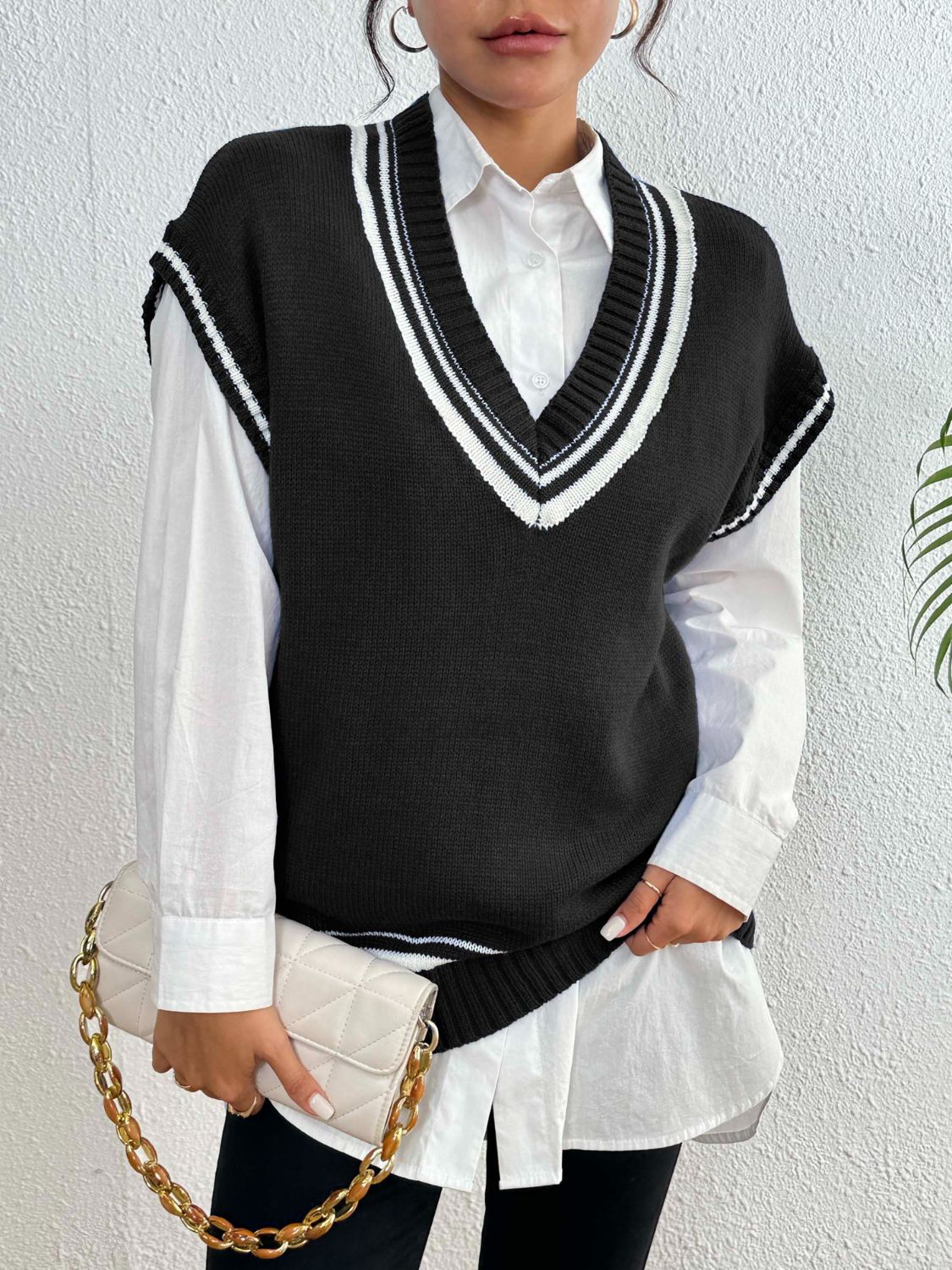 Black acrylic knit vest with white contrast trim, V-neck, sleeveless, layered over a white collared shirt.