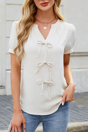 Cream textured V-neck blouse with three bow details and short sleeves.