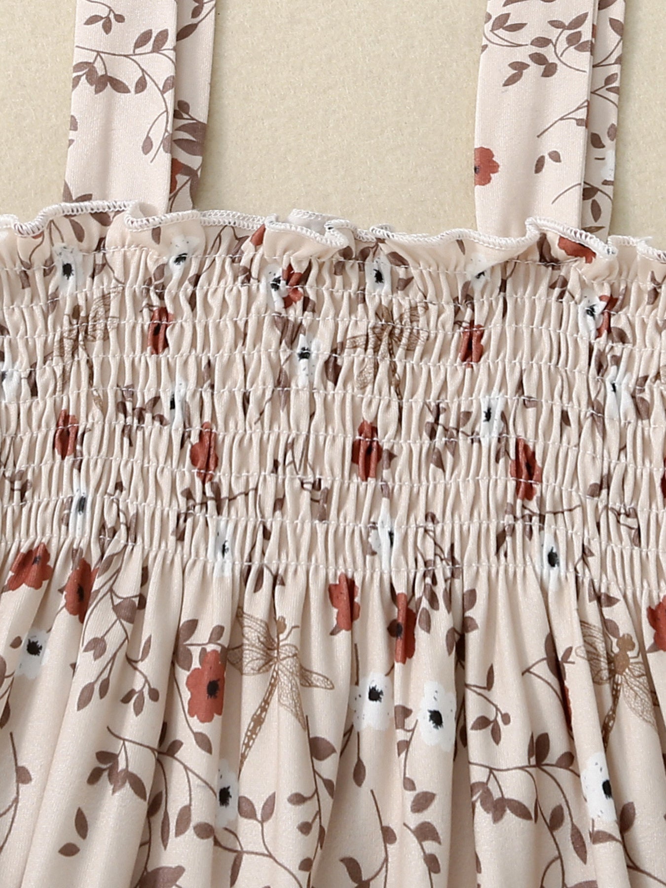 Baby jumpsuit with apricot floral print, smocked bodice, and ruffled neckline.