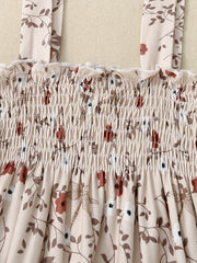 Baby jumpsuit with apricot floral print, smocked bodice, and ruffled neckline.