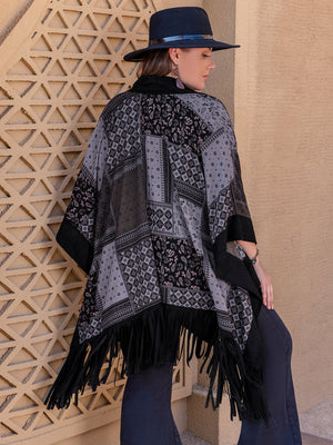 Black patchwork print kimono with fringe detail and wide sleeves, styled with a hat.