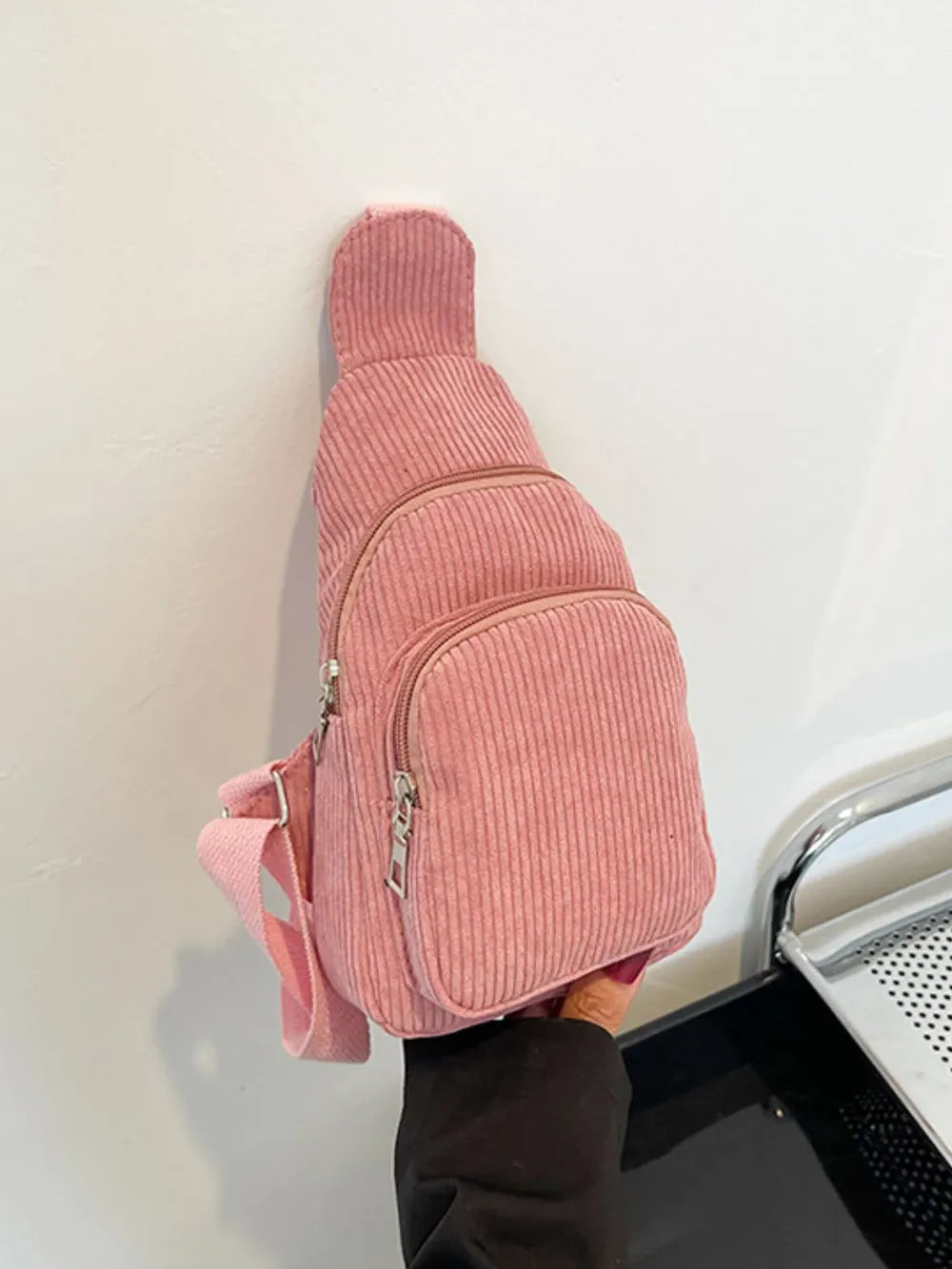 Pink corduroy sling bag with zip pockets and adjustable strap.