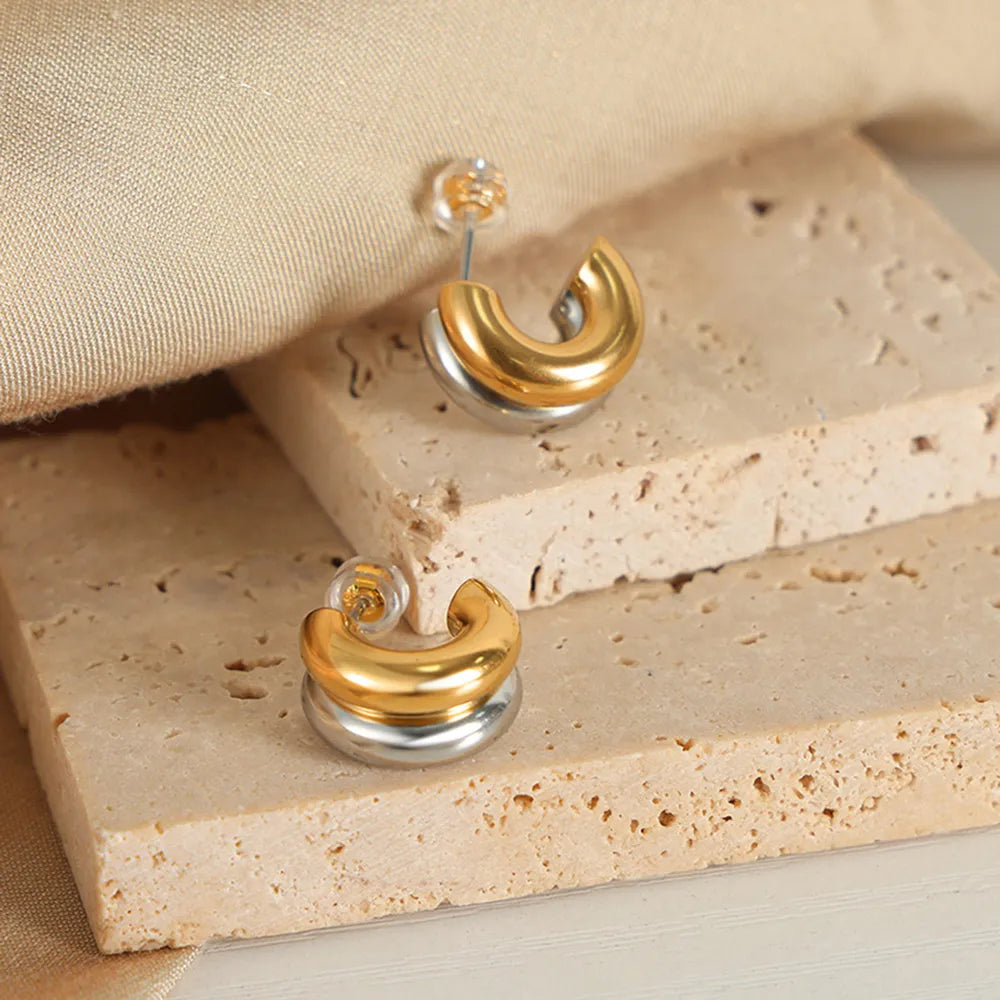 Dual-tone sculptural C-hoop earrings in gold and silver with a polished finish.
