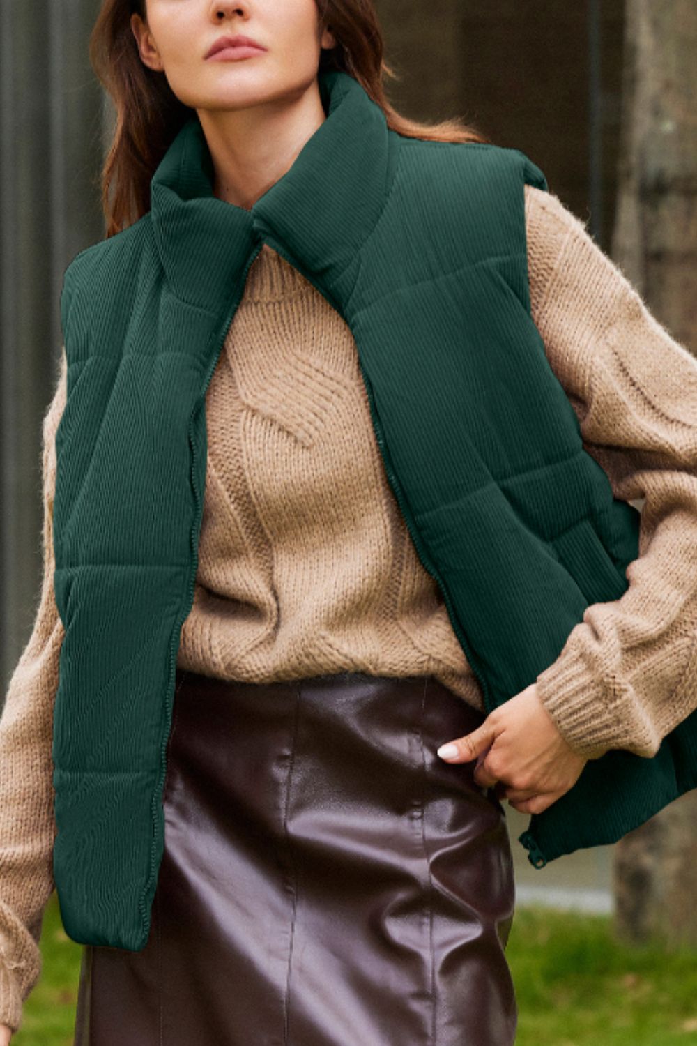 Dark green corduroy padded vest with a high collar, worn over a tan cable knit sweater.