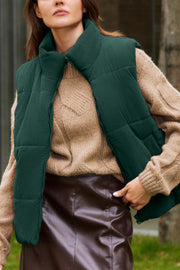 Dark green corduroy padded vest with a high collar, worn over a tan cable knit sweater.