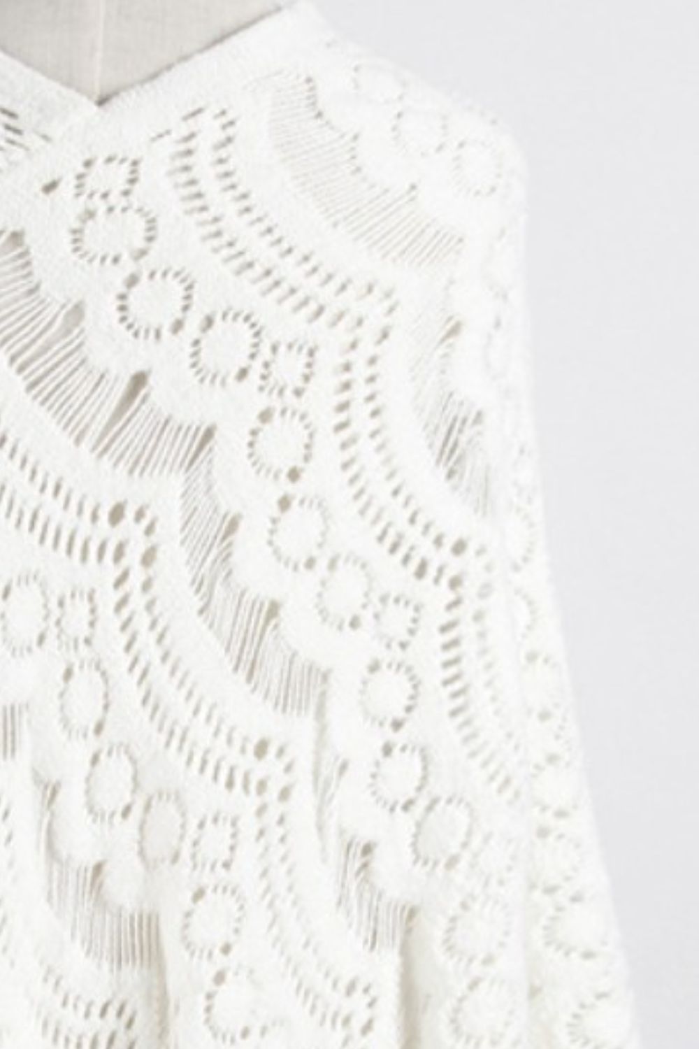White crochet poncho with intricate openwork pattern and fringe detail.