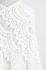 White crochet poncho with intricate openwork pattern and fringe detail.