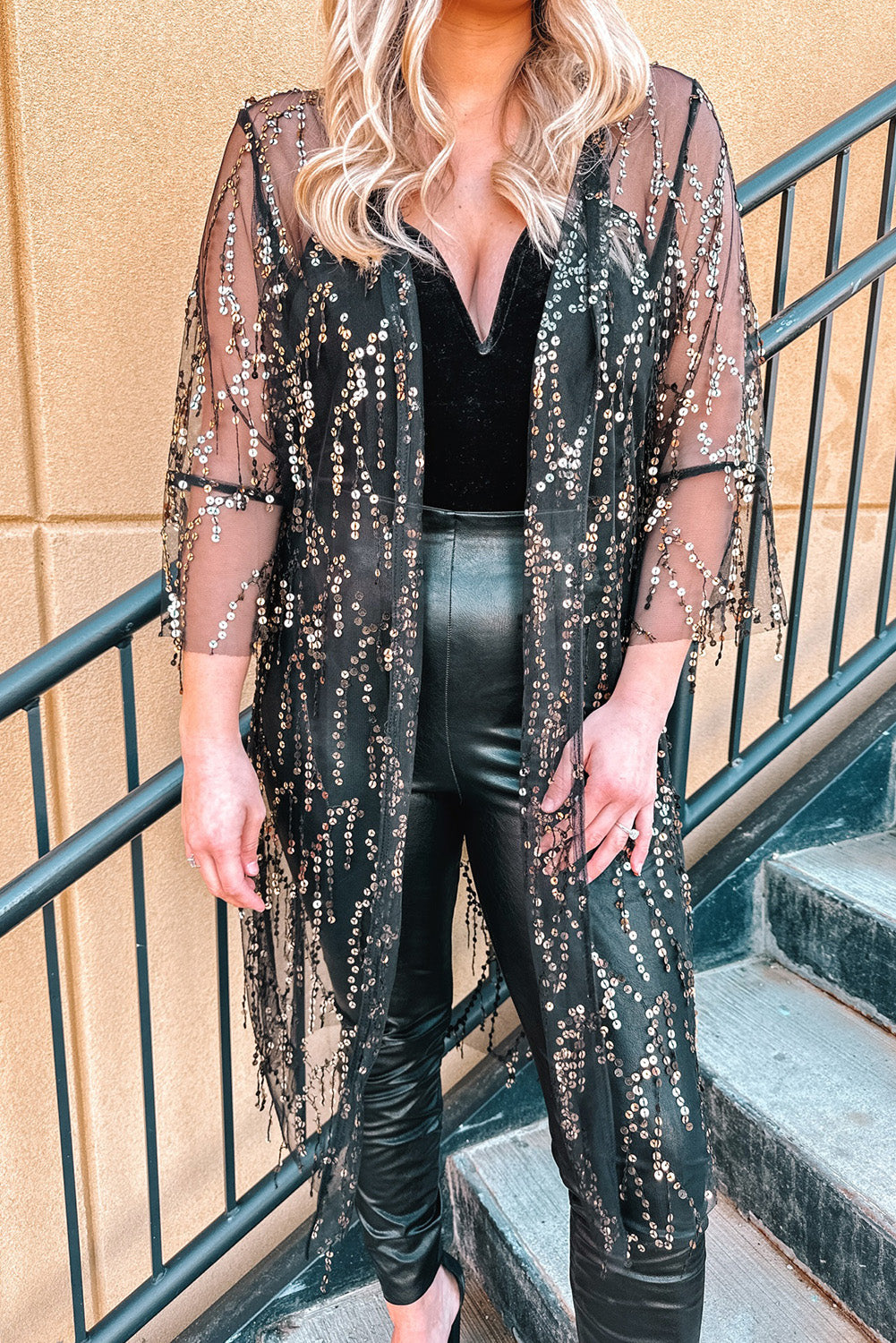 Black sequin duster with flared sleeves and fringe hem, worn over a black velvet bodysuit and faux leather pants.