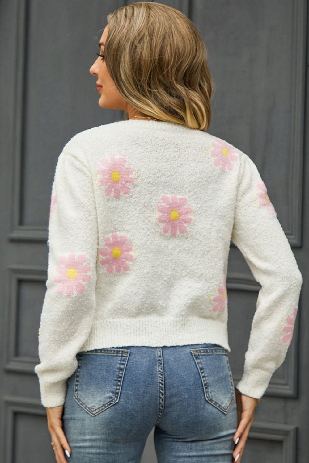 White textured knit sweater with pink daisy motif and yellow centers.