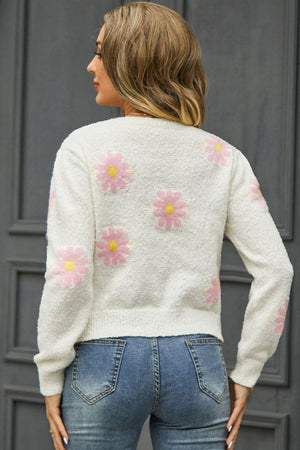White textured knit sweater with pink daisy motif and yellow centers.