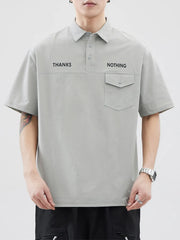 Light gray polo shirt with button detail, chest pocket, and text graphic.