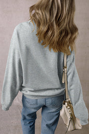 Gray cotton sweatshirt with long sleeves and a crew neck, styled with jeans and a crossbody bag.