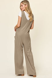 Mocha wide-leg pocket jumpsuit with deep V-neck and sleeveless design, styled over a white tee.