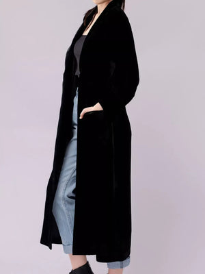 Black velvet longline trench coat with draped lapels and side slits.