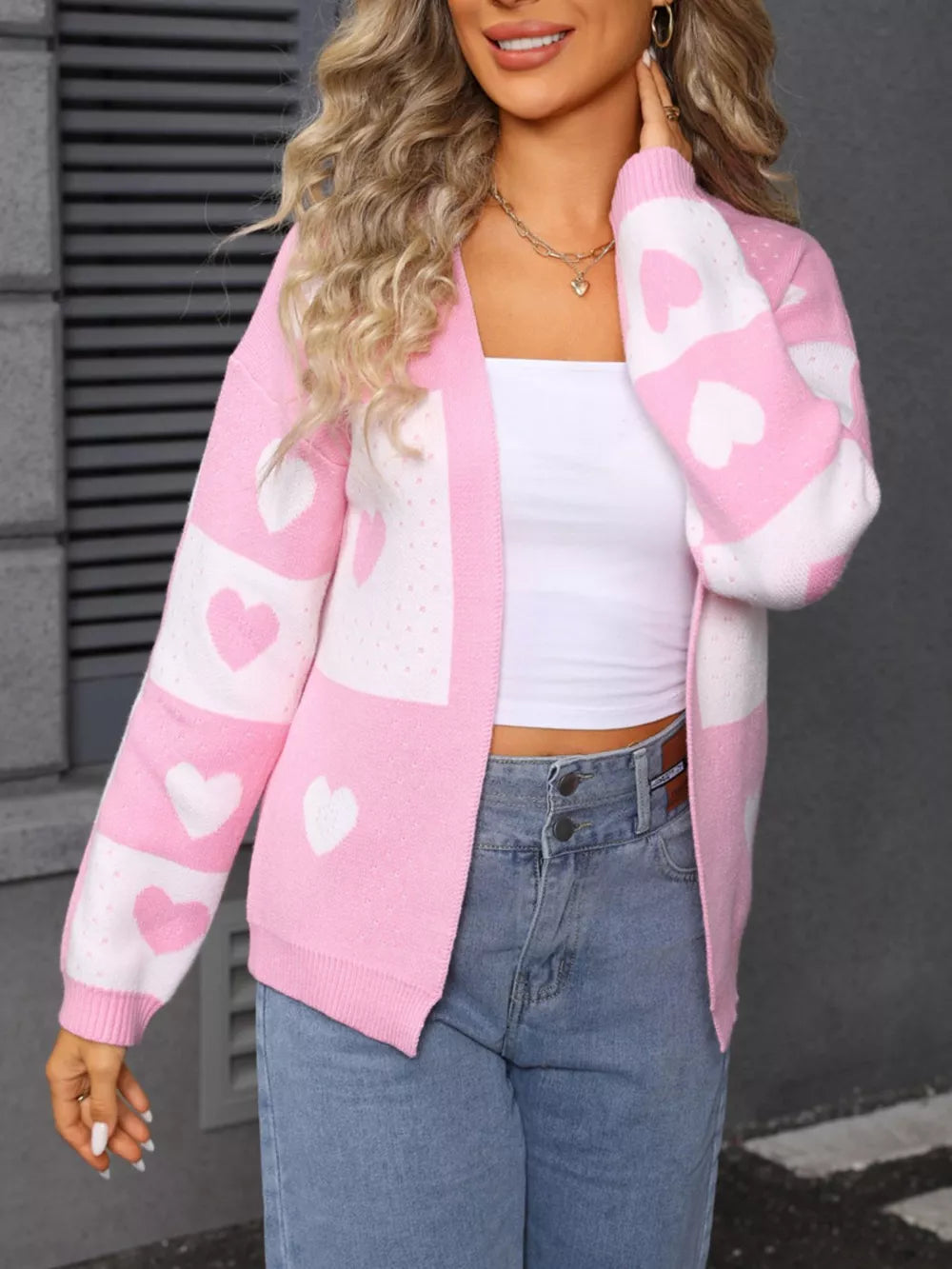 Blush pink acrylic cardigan with white heart motif and open front.