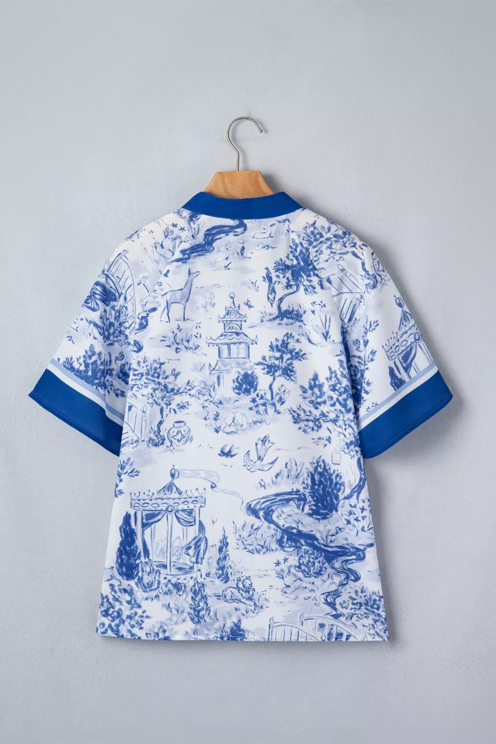 White polyester shirt with blue toile print, V-neck, short sleeves, and blue trim.