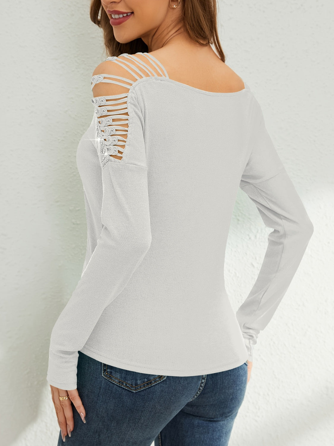 White ribbed knit blouse with strappy cold shoulder detail and embellished accents.
