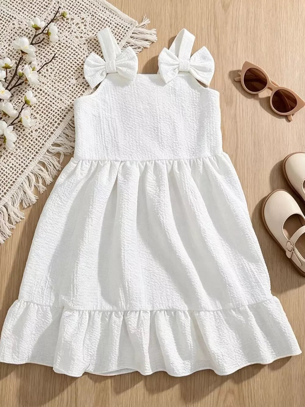 White baby dress with bowknot straps, textured fabric, and ruffle hem.