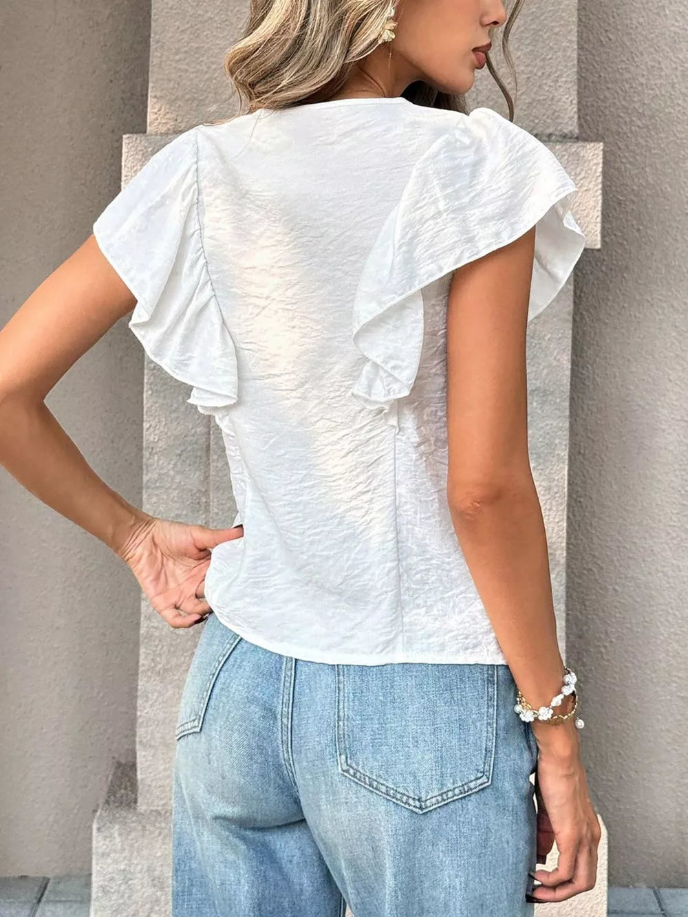White ruffled V-neck shirt with textured fabric and flutter sleeves.