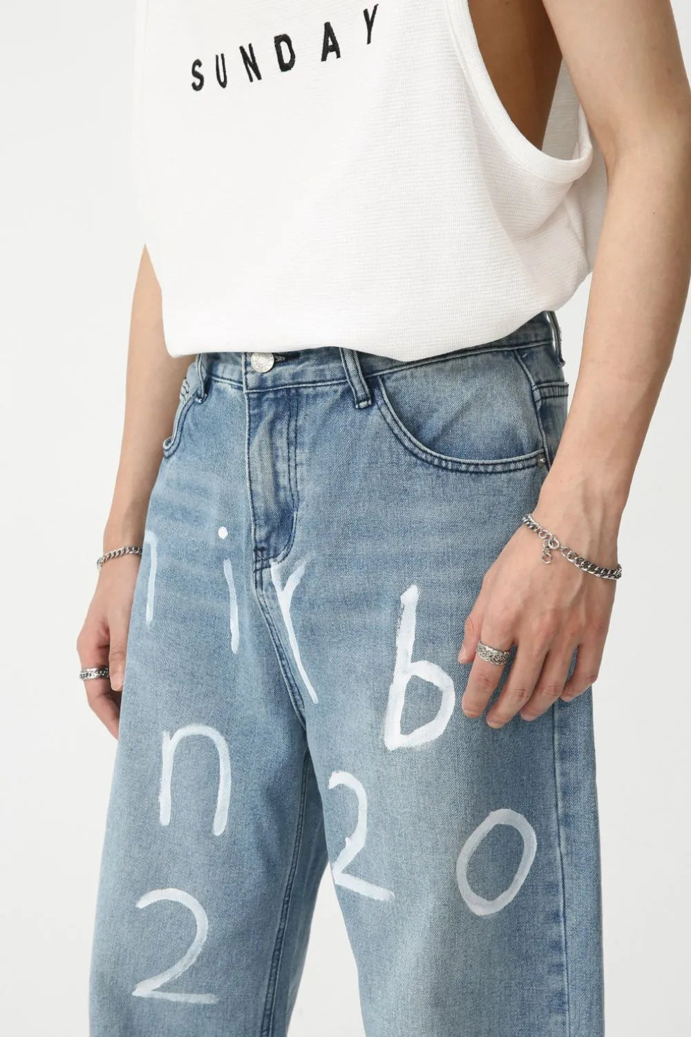 Medium wash baggy jeans with white painted script detail, casual style.