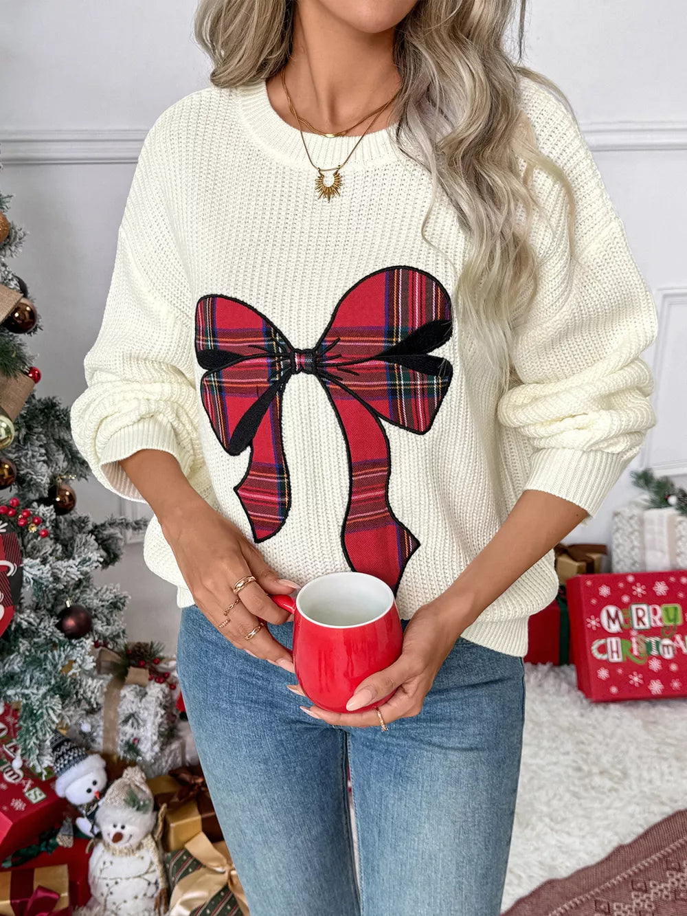 Cream ribbed knit sweater with a large red plaid bow detail, crew neck.