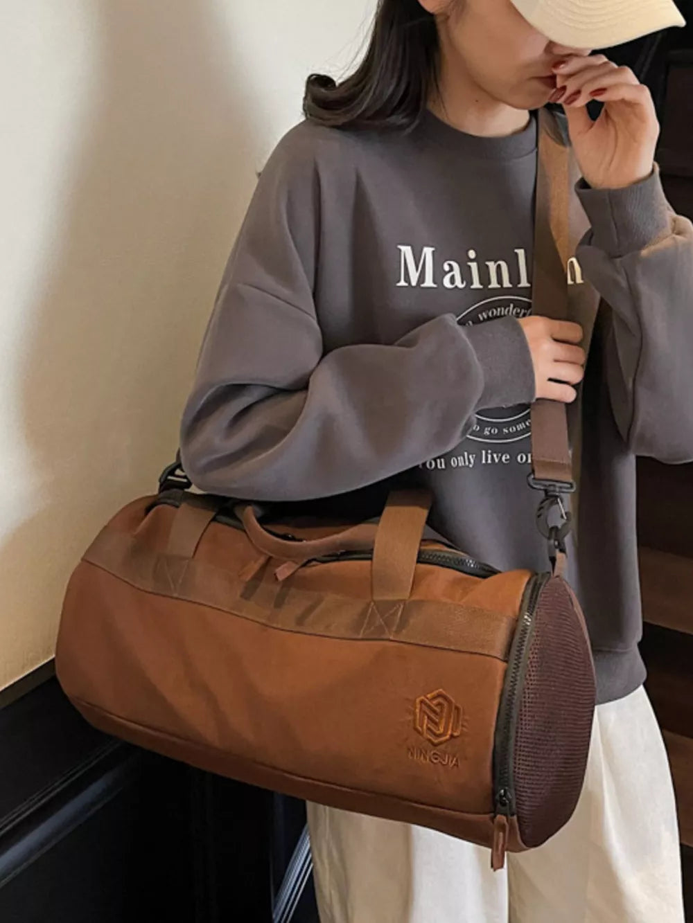 Brown Oxford cloth duffel bag with carry handles and adjustable strap, featuring mesh end caps.