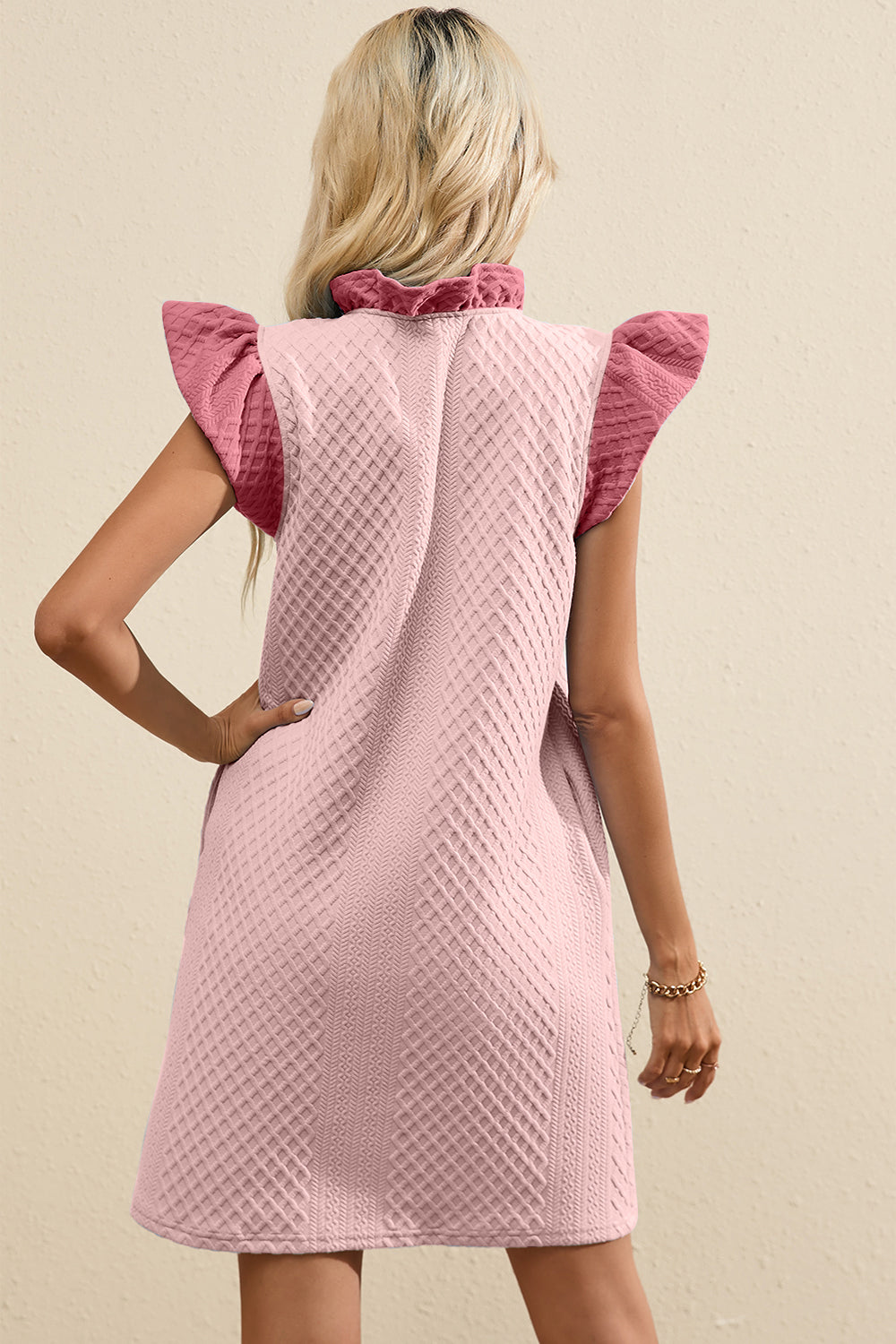 Blush pink trapeze dress with textured fabric, ruffled mock neck, and flutter sleeves.