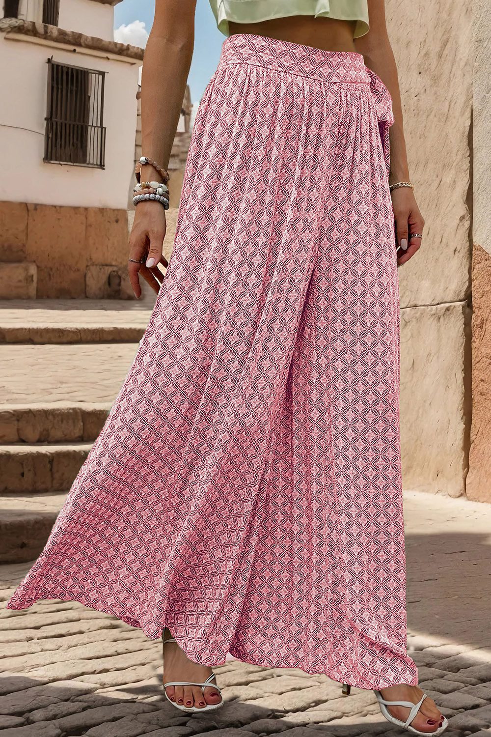 Pink geometric print wide-leg palazzo trousers with a tie waist, styled with white sandals.