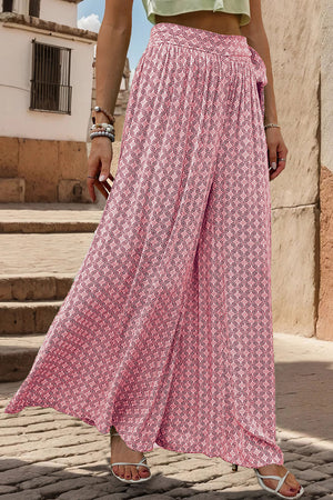 Pink geometric print wide-leg palazzo trousers with a tie waist, styled with white sandals.