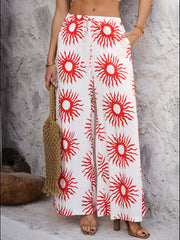Geometric print wide-leg trousers in white with red suns, drawstring waist, and pockets.