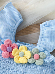 Pastel blue smocked jumpsuit with floral appliques and ruffled sleeves.