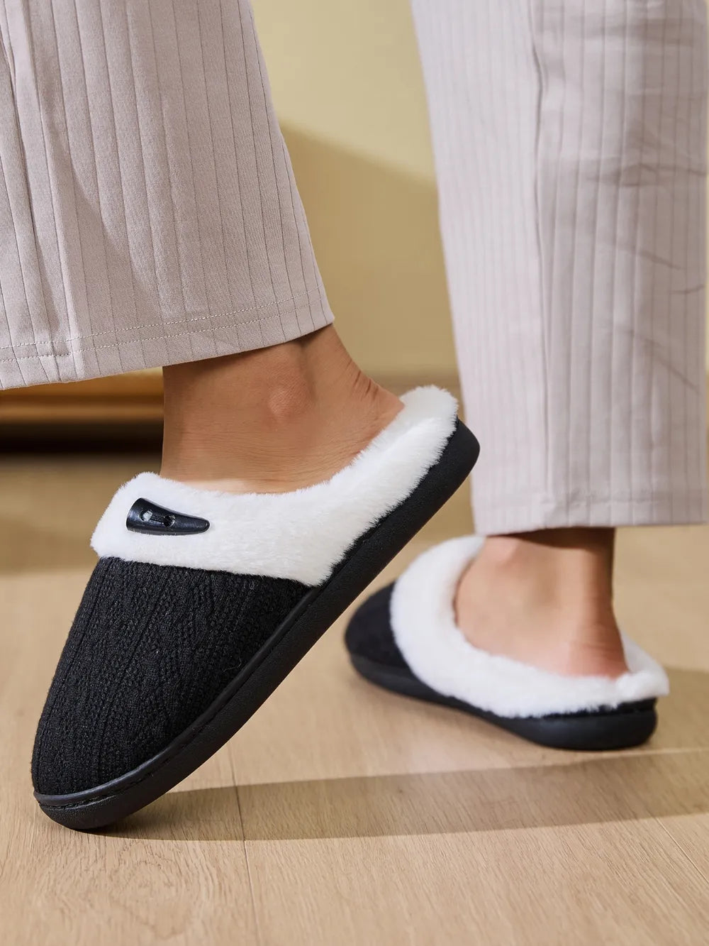 Black cable knit house slippers with white shearling lining and a decorative button detail.