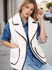 White sherpa vest coat with black contrast trim and button front, worn over denim.