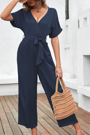 Navy crossover neckline fluid wide leg jumpsuit with belted waist and short sleeves.