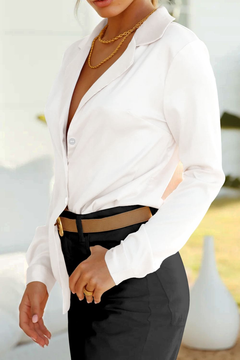 White satin blouse with poet sleeves and button detail, styled with black pants and a tan belt.