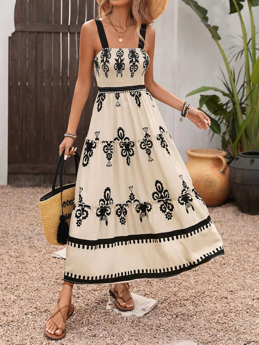 Bohemian smocked maxi dress in cream with black floral print, tiered skirt, and black straps.