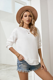 White crewneck sweatshirt with asymmetric hemline and long sleeves, styled with denim shorts.