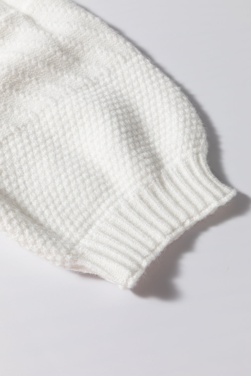 White cable knit sweater sleeve with ribbed cuff and diamond texture detail